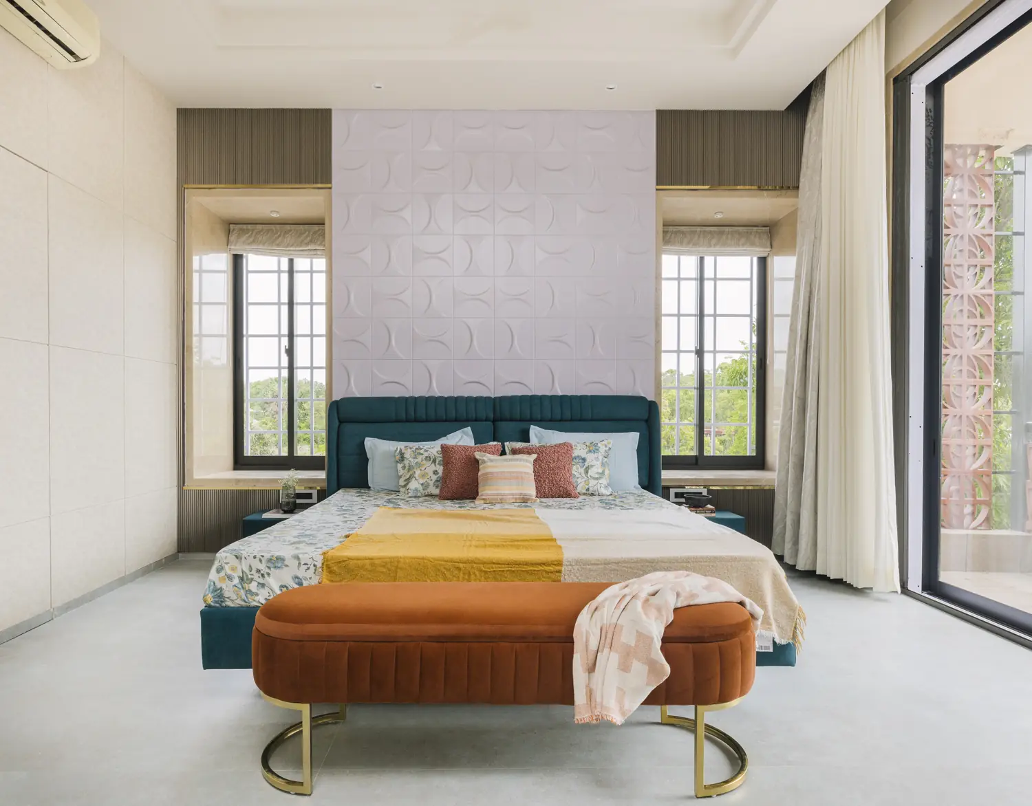 Bedroom with a teal upholstered bed, rust bench and lilac relief wall